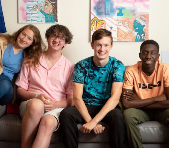 Four young carers sit on a sofa smiling at the camera